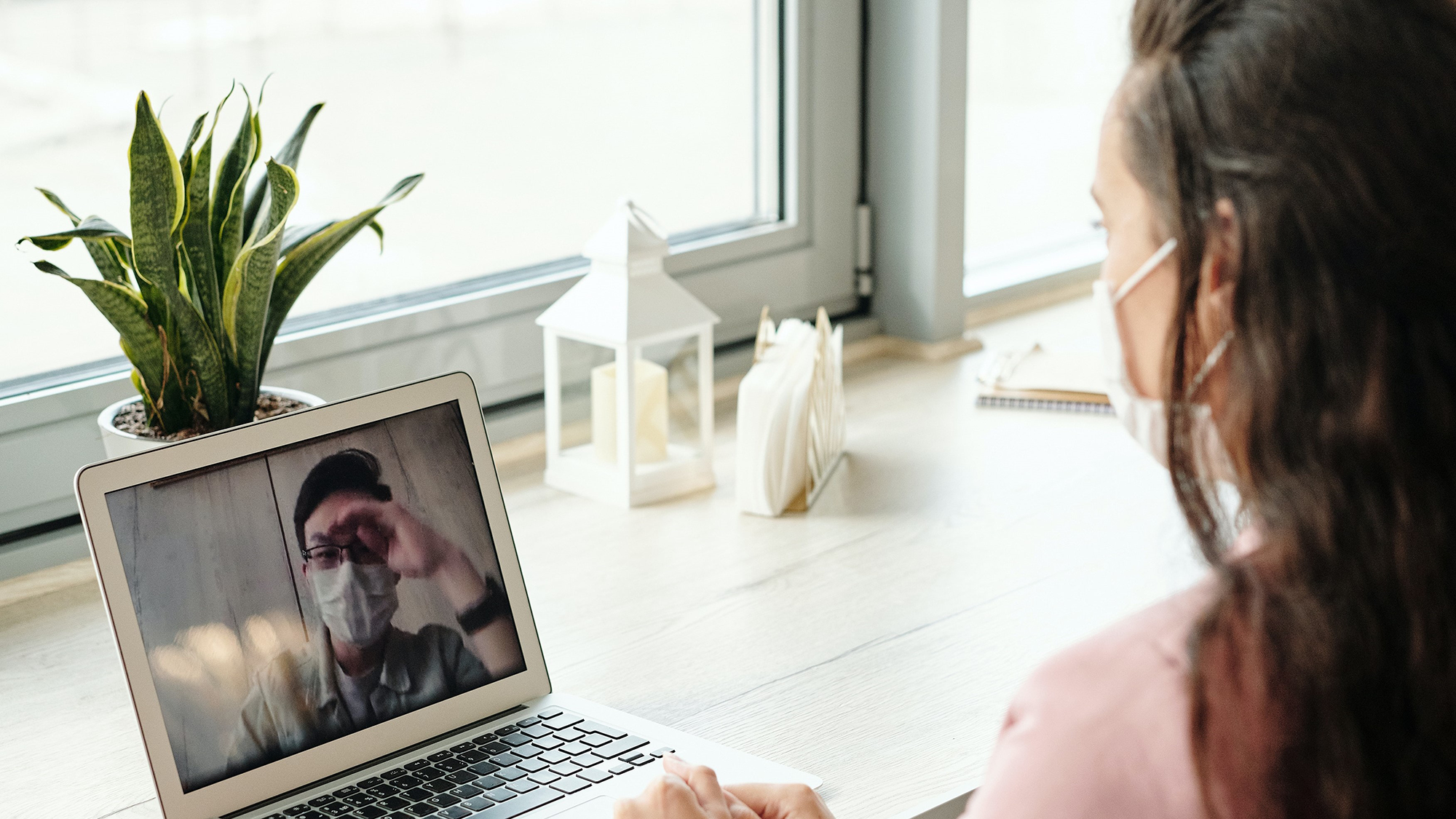 Woman on her laptop, wearing a mask, and video chatting with a man also wearing a mask